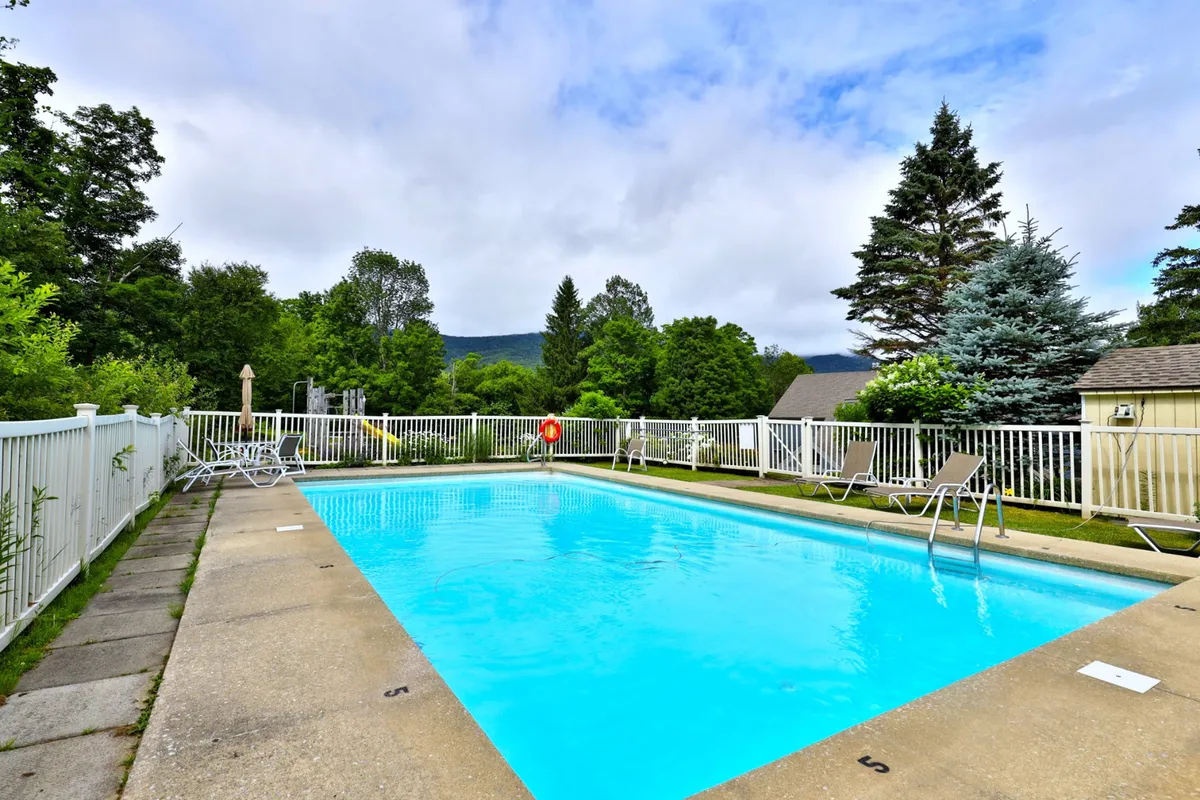 This image features the outdoor swimming pool surrounded by lush green landscaping and poolside lounge chairs, evoking the fun and relaxation of warm summer days. The setting is ideal for family swims, lazy afternoons, or playful gatherings.