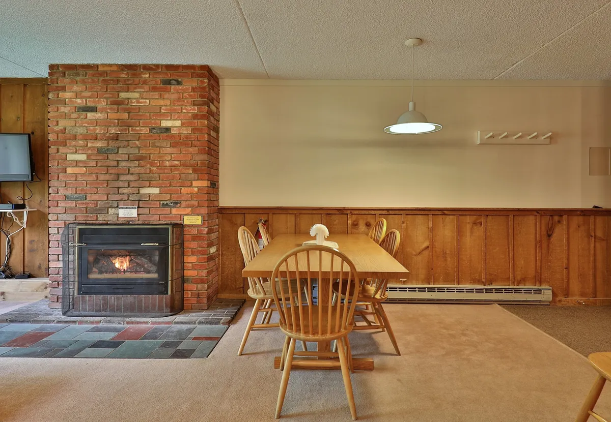 A cozy interior space centered around a brick fireplace with a dining table and wooden chairs. The ambience is warm and inviting, ideal for gathering with friends or relaxing by the fire during chilly evenings.
