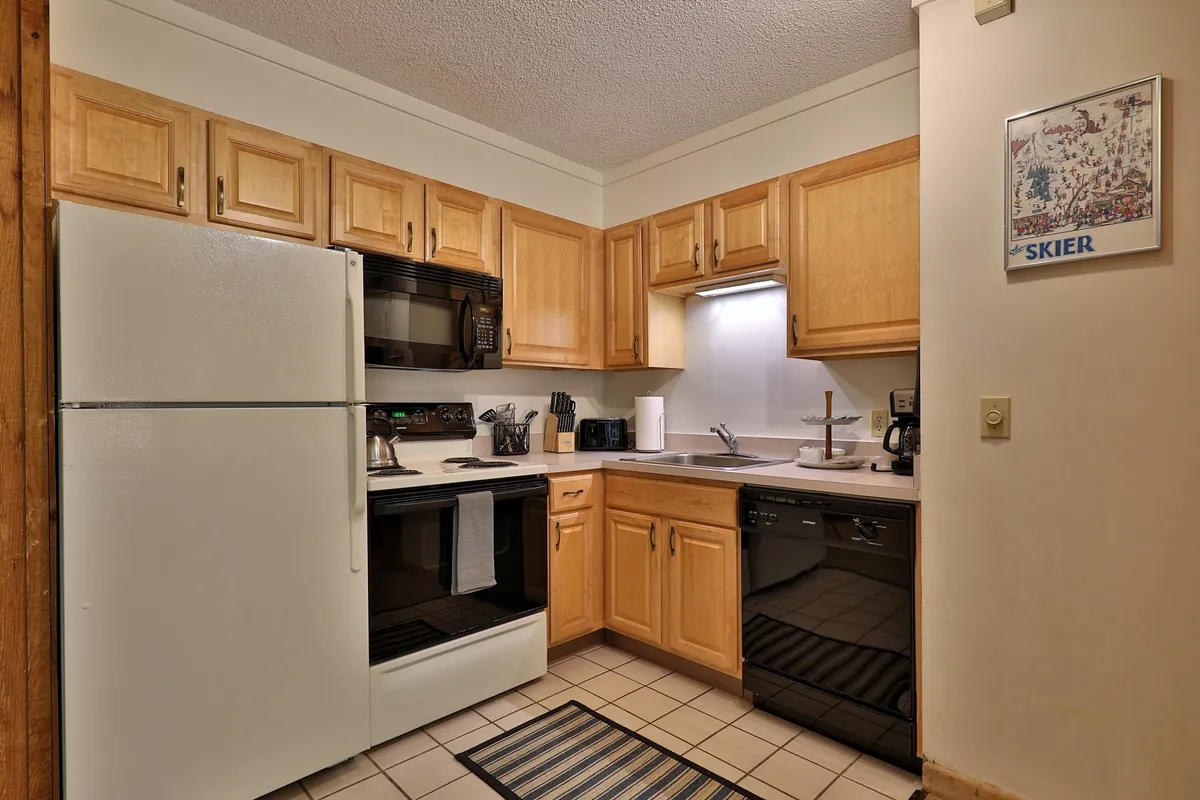 A welcoming kitchen space featuring modern appliances, wooden cabinetry, ample counter space, and a decorative ski poster that adds a touch of local flavor. The kitchen is well-lit and organized, ideal for cooking and gathering.