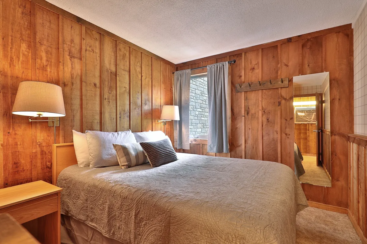 A bright bedroom with a bed positioned to capture sunlight filtering through a window. The space is accentuated by textured walls and stylish lighting fixtures, creating an inviting place to wake up or relax with a book.