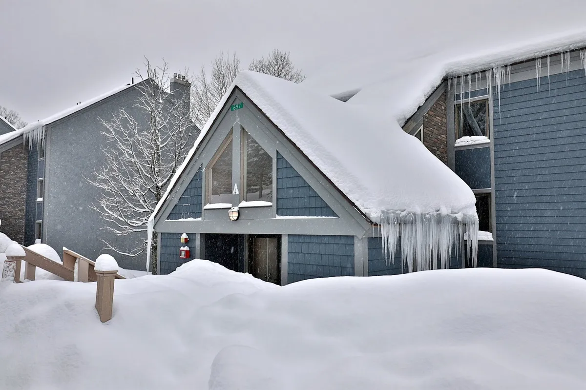 A peaceful exterior shot of the condo building with a snow-laden landscape, icicles glistening along the roofline, and a sturdy wooden railing. The overall mood is tranquil, evoking crisp winter days and the anticipation of returning to warmth indoors after an active day outside.