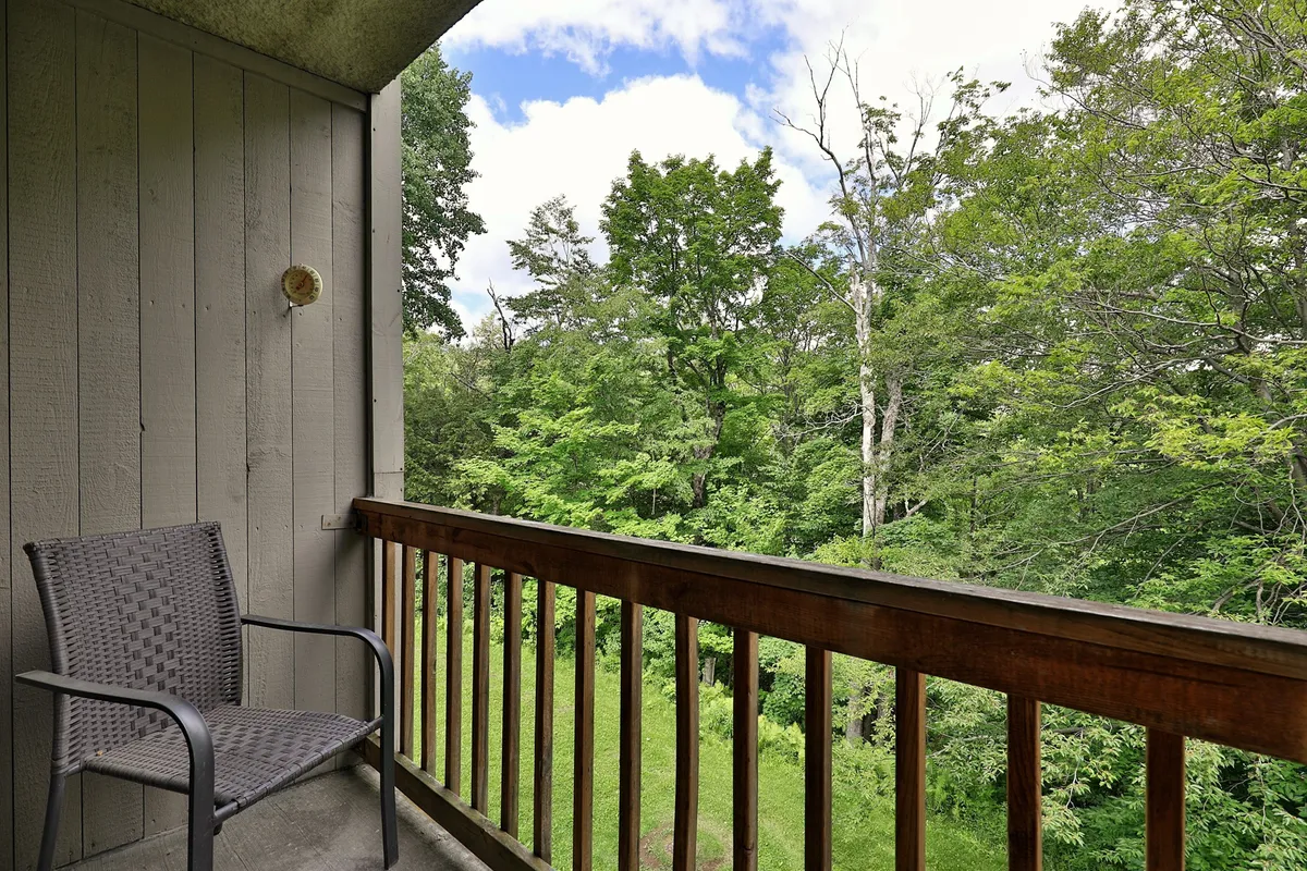 A tranquil private balcony with a sturdy railing and an outdoor chair, surrounded by lush greenery. The scene suggests a peaceful spot for morning coffee or evening drinks while enjoying Vermont’s natural beauty.