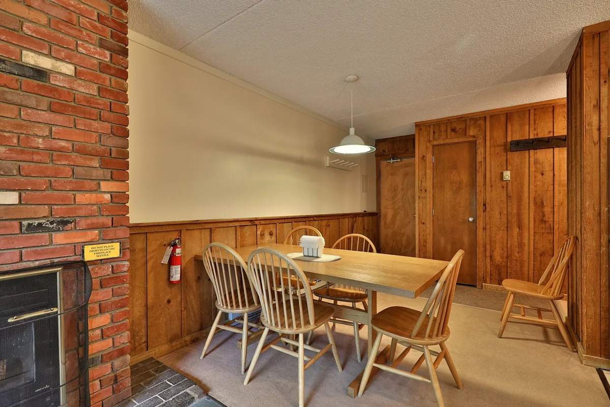 A warm, inviting dining area features a wooden table, a prominent brick fireplace, and a stylish pendant light. This space evokes the cozy ambiance awaiting after a day spent exploring Vermont’s outdoor playground.