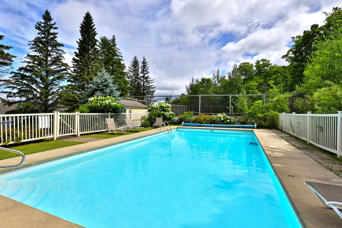 A sparkling outdoor swimming pool surrounded by lush greenery and a secure fence. Lounge chairs line the pool's edge, inviting guests to relax, sunbathe, or socialize in the warm weather. The setting conveys a carefree, resort-style atmosphere.