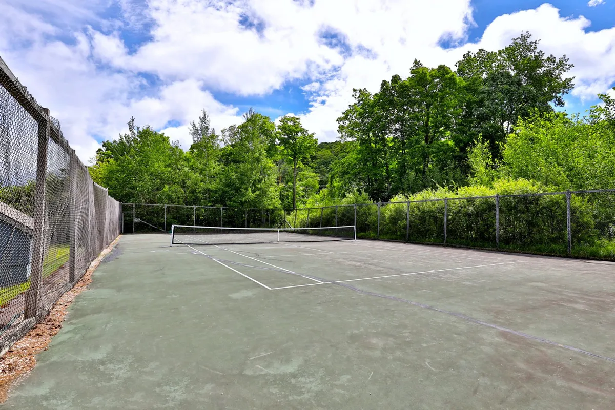 A tennis court surrounded by lush greenery, fenced in for safety and privacy. The scene radiates with energy and the possibility of group activities and friendly competitions right at your doorstep.