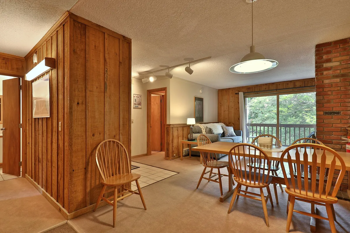 A spacious dining area anchored by a table set for six, with a comfortable sofa nearby and a large window that brings in natural light. The arrangement invites guests to linger over meals, play games, or relax together.