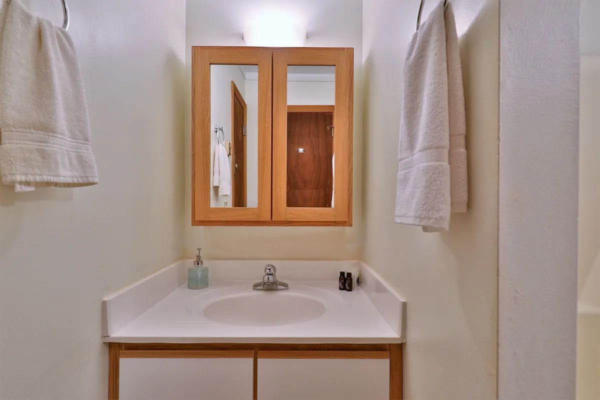 A tranquil, tidy bathroom featuring a sink with mirror, neatly arranged towels, and wooden cabinetry. The soft lighting and natural elements contribute to a calming atmosphere, perfect for morning or evening routines.
